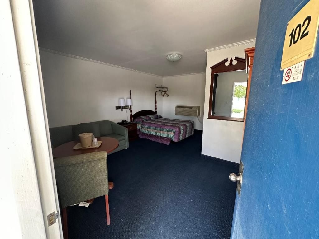 Quarto com cama, poltrona, mesa com abajur e espelho na parede.
