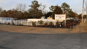 Un letrero que dice 'Four Oaks RV Resort', con una valla blanca y árboles de fondo.