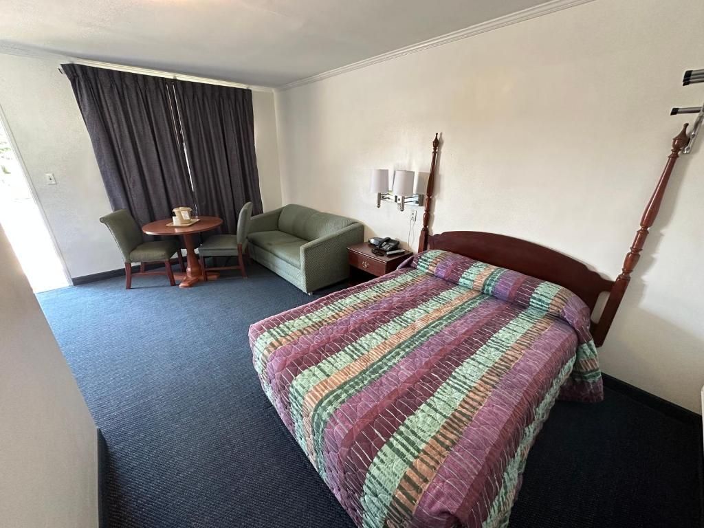 Una camera d'albergo con un letto, una poltrona verde, un tavolino rotondo e una lampada.