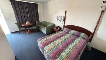 Una camera d'albergo con un letto, una poltrona verde, un tavolino rotondo e una lampada.