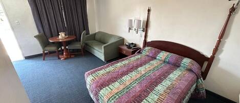 A hotel room with a bed, a green armchair, a small round table, and a lamp.