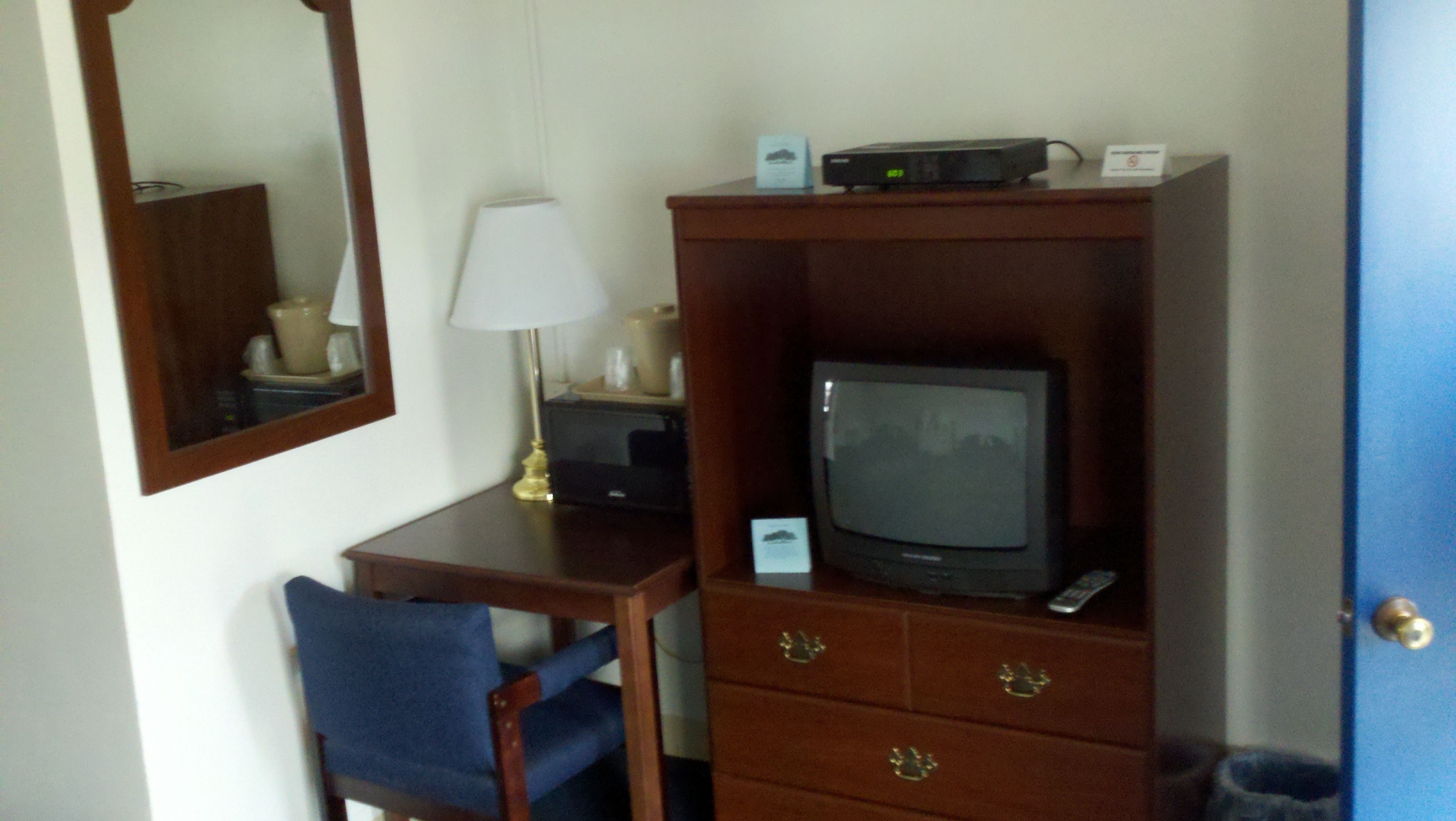 A hotel room with a wooden desk, a television, a lamp, and a mirror.