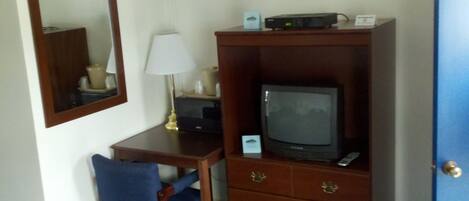 A hotel room with a wooden desk, a television, a lamp, and a mirror.