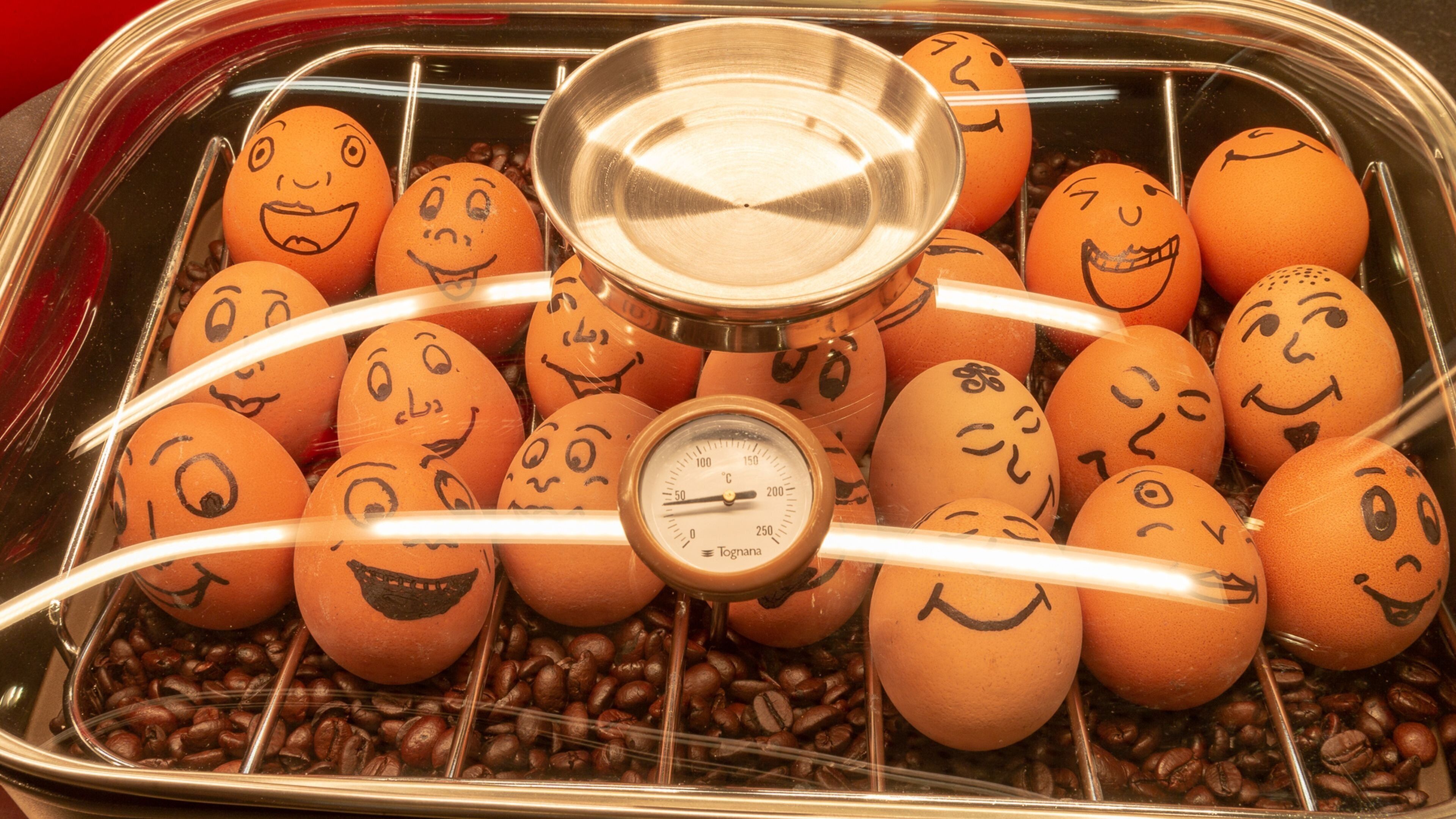 Un vassoio con uova che hanno delle facce, circondato da chicchi di caffè.