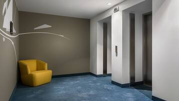 Et hotelmødested med en gul stol, et blå mønstret tæppe og en væg med et hvidt abstrakt design.