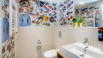 A bathroom with a white sink, toilet, and shower area. The walls are decorated with various photos and stickers.