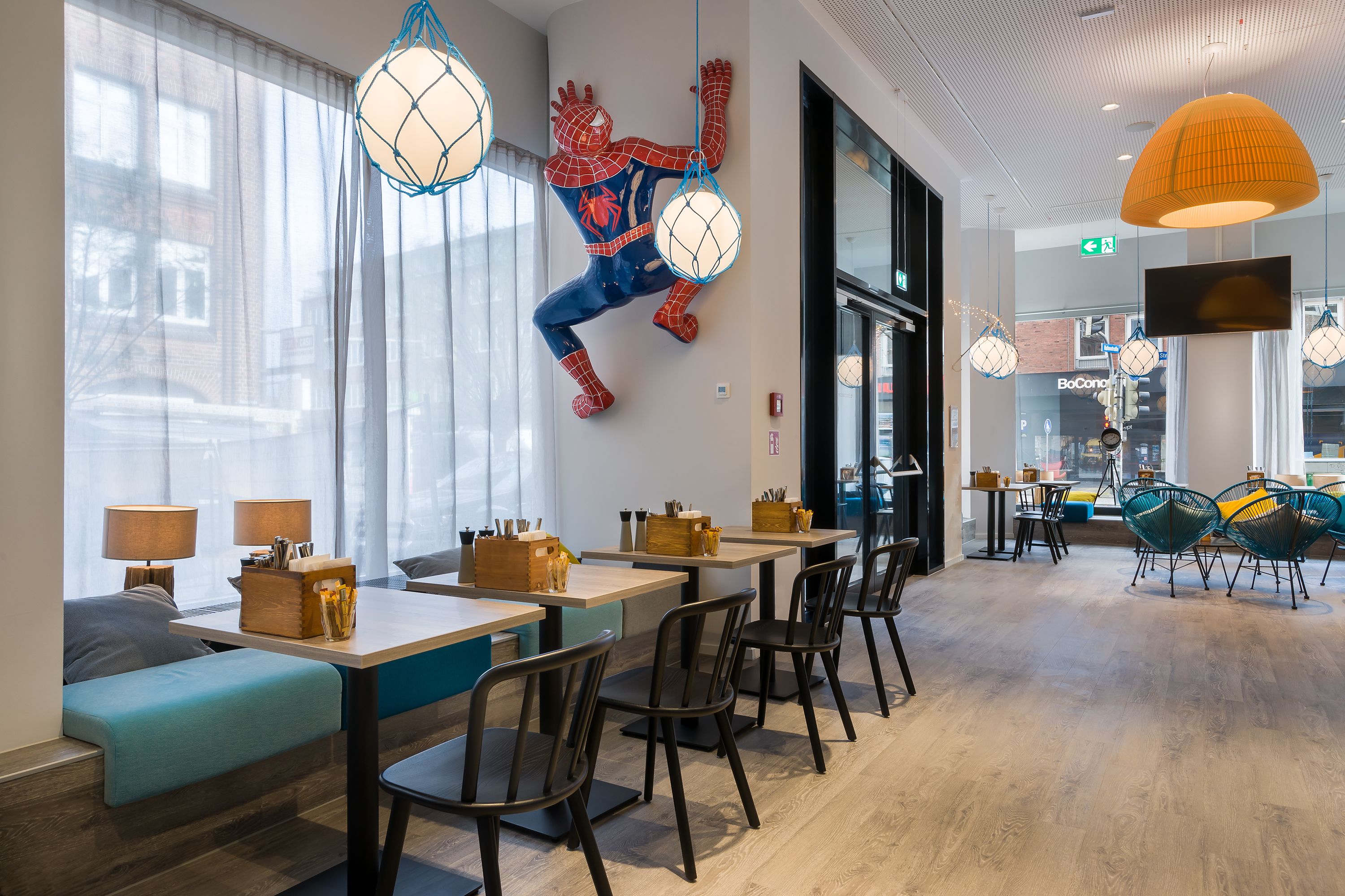 A modern restaurant with a Spider-Man mural, wooden tables, and black chairs.
