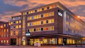 Un hotel de varios pisos con fachada de ladrillo moderno, ventanas iluminadas y un letrero que indica 'the niu' en la esquina.