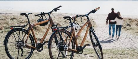 Two bicycles parked on a sandy beach with a couple walking in the background.