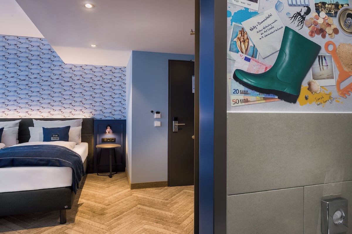 A hotel room with a bed, a small table, and a wall decorated with various items including a green boot, coins, and a lighthouse picture.