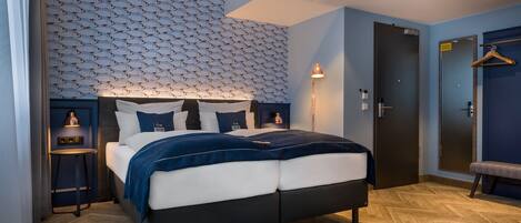 A modern hotel room with a bed, a small table, a bench, and a wardrobe.