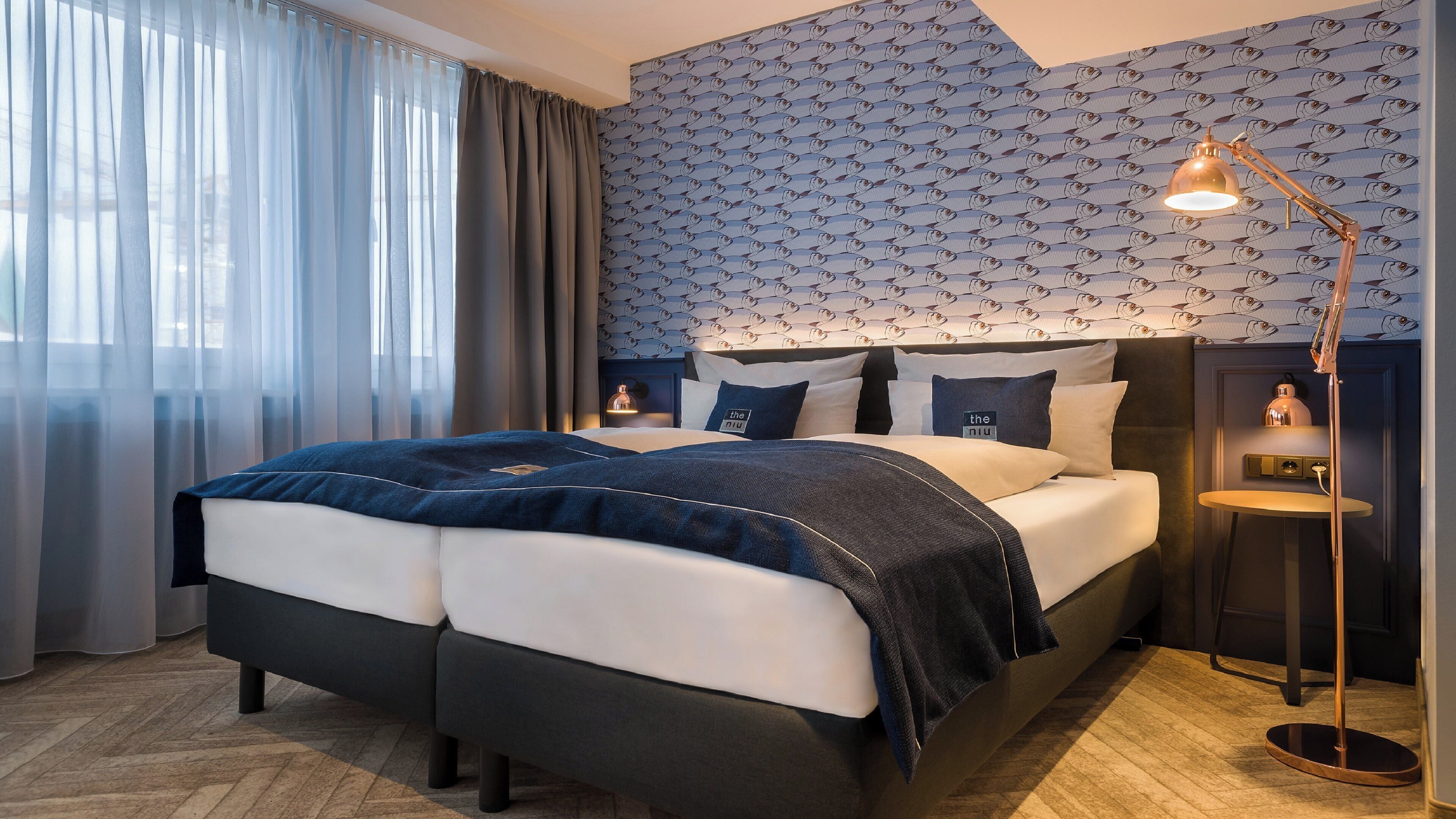 A modern hotel room with a large bed, a nightstand, and a wall-mounted lamp.