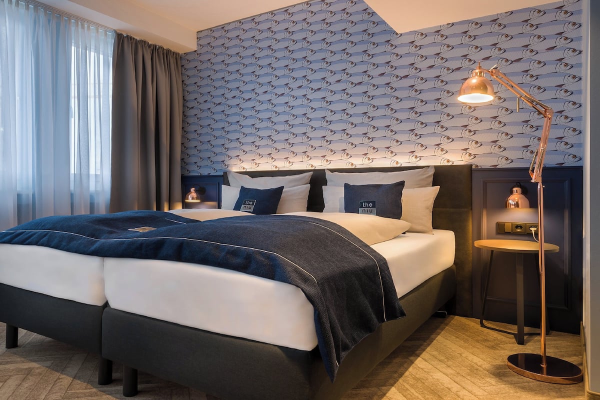 A modern hotel room with a large bed, a nightstand, and a wall-mounted lamp.