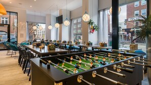 Un espacio interior moderno con mesa de fútbol, zona de estar y ventanas amplias con vistas a la ciudad.