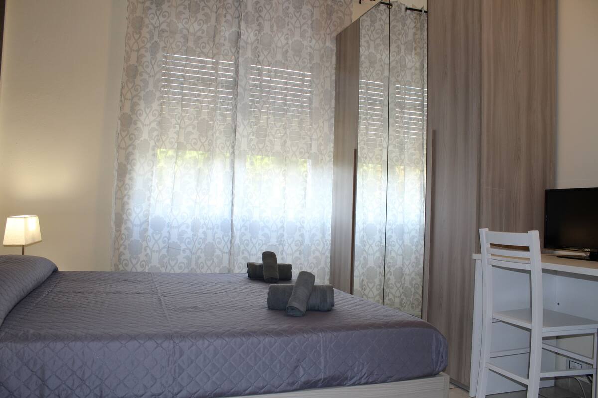 A bedroom with a bed, a desk, a chair, and a TV.