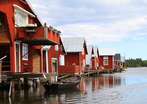 A row of red wooden houses with a dock extending into calm water, boats moored at the dock, and a clear sky above. - Hotel Mellanfjärden (Jättendal)