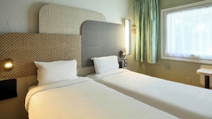 Ein Hotelzimmer mit zwei Betten, einem Kopfteil mit Strukturmuster, einem Nachttisch mit Lampe und einem Fenster mit Vorhängen.
