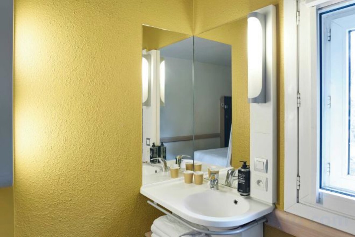 A bathroom with a white sink, a mirror, and a window.