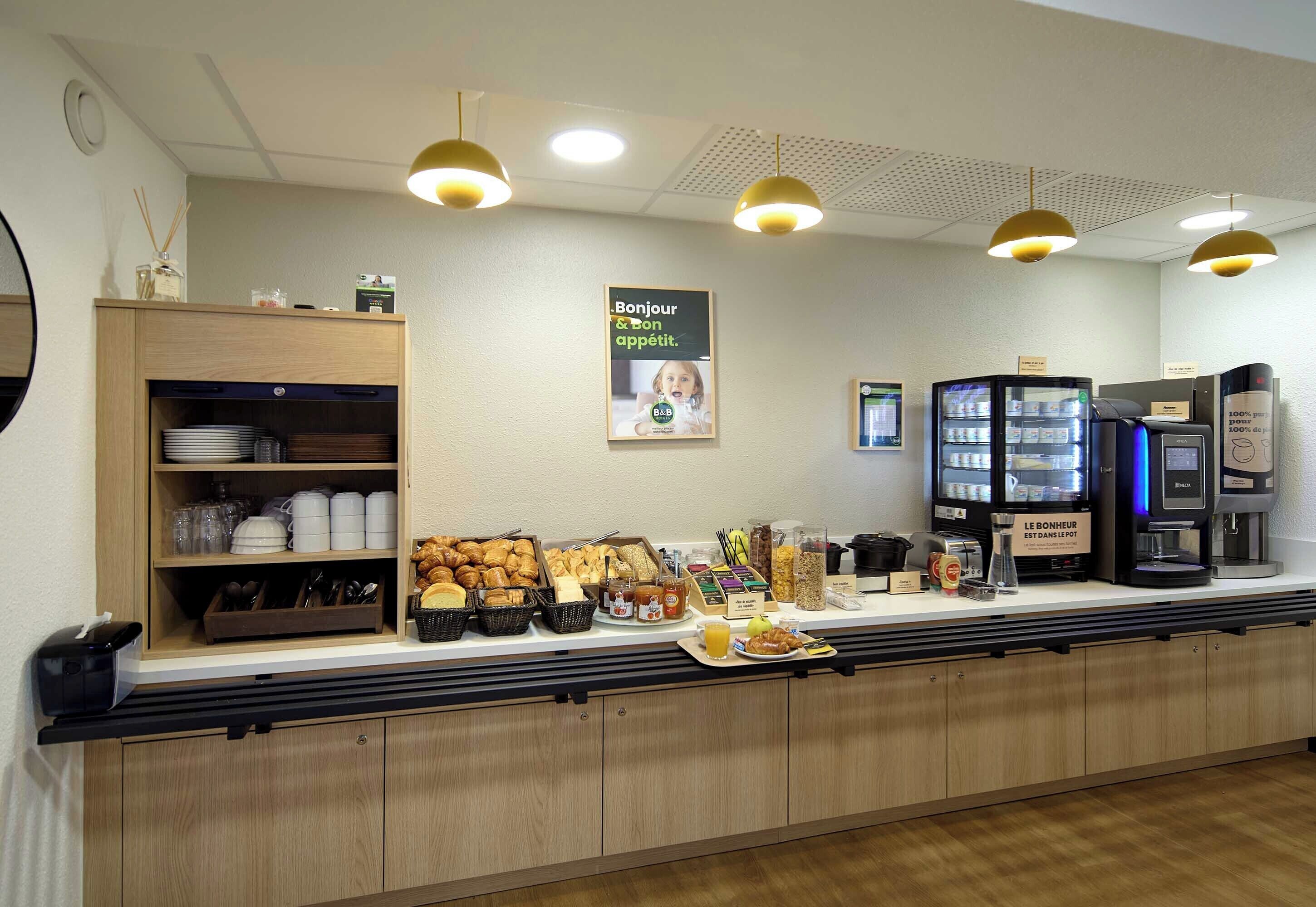 A breakfast bar with a variety of food items, a coffee machine, and a refrigerator.
