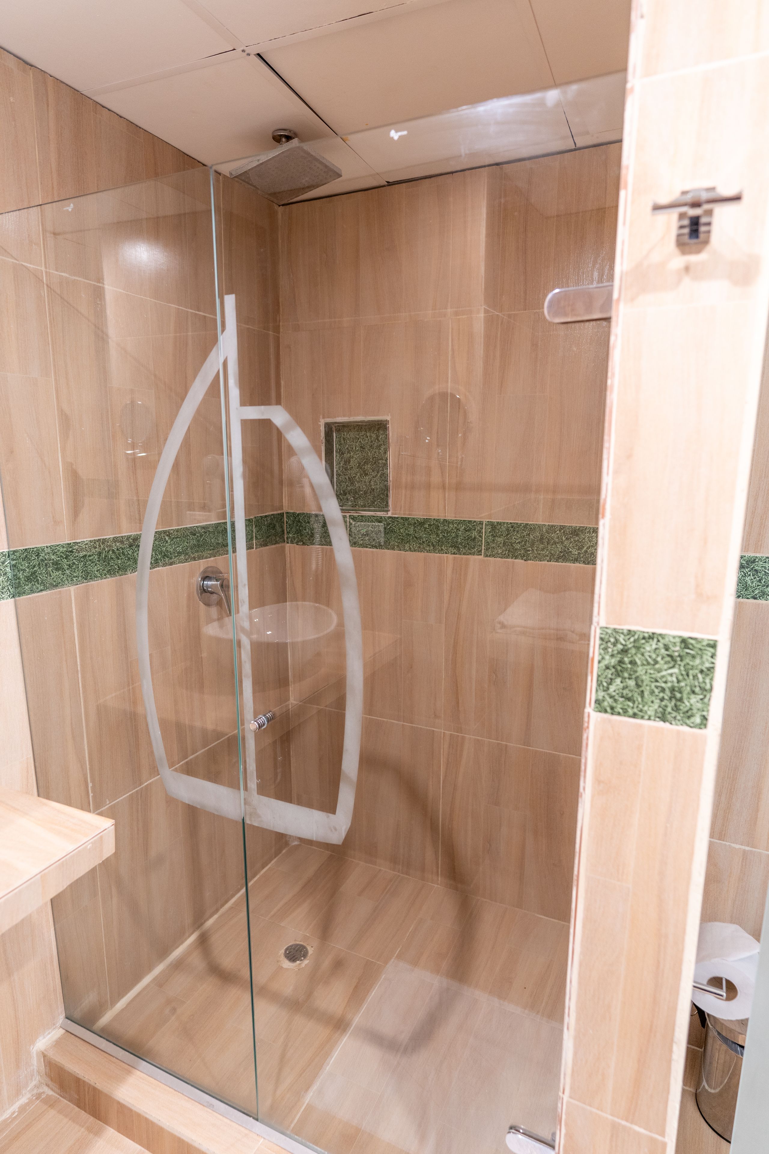 Une douche entièrementClose avec des parois en verre, un sol en bois et des touches de couleur grâce à des carreaux verts.
