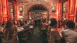Un restaurant aux murs de briques, aux poutres apparentes et agrémenté d’un lustre. Les tables sont disposées et les clients sont assis, prêts à dîner.