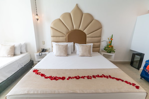 Una habitación de hotel con una cama grande, un cabecero decorativo, una mesita de noche con una lámpara y una planta pequeña en el buró.