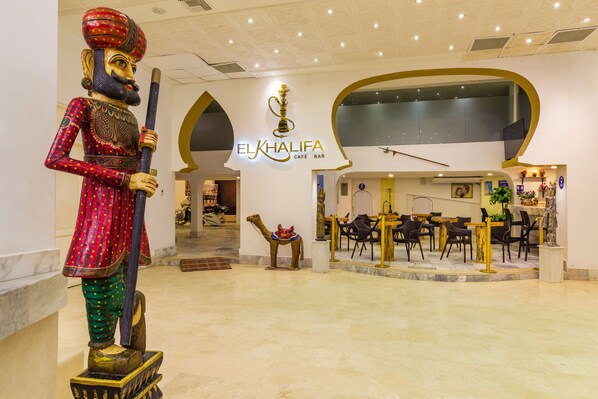 Un interior moderno con una estatua, un bar cafetería y una zona de recepción.