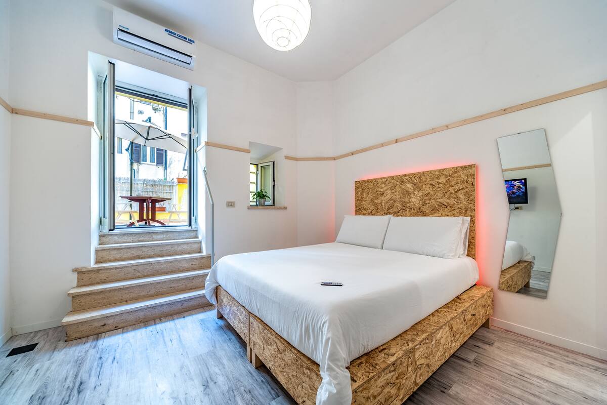 A modern bedroom with a large bed, a window with a view, and a wooden headboard.