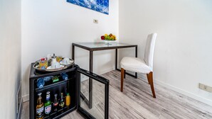 Una habitación con una mesita de vidrio que sostiene un frutero, una silla blanca y un minibar con diferentes bebidas.