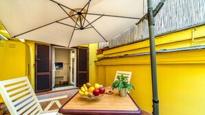 Un patio exterior pintado de amarillo con una mesa, sillas, un cuenco de frutas y una planta en maceta.