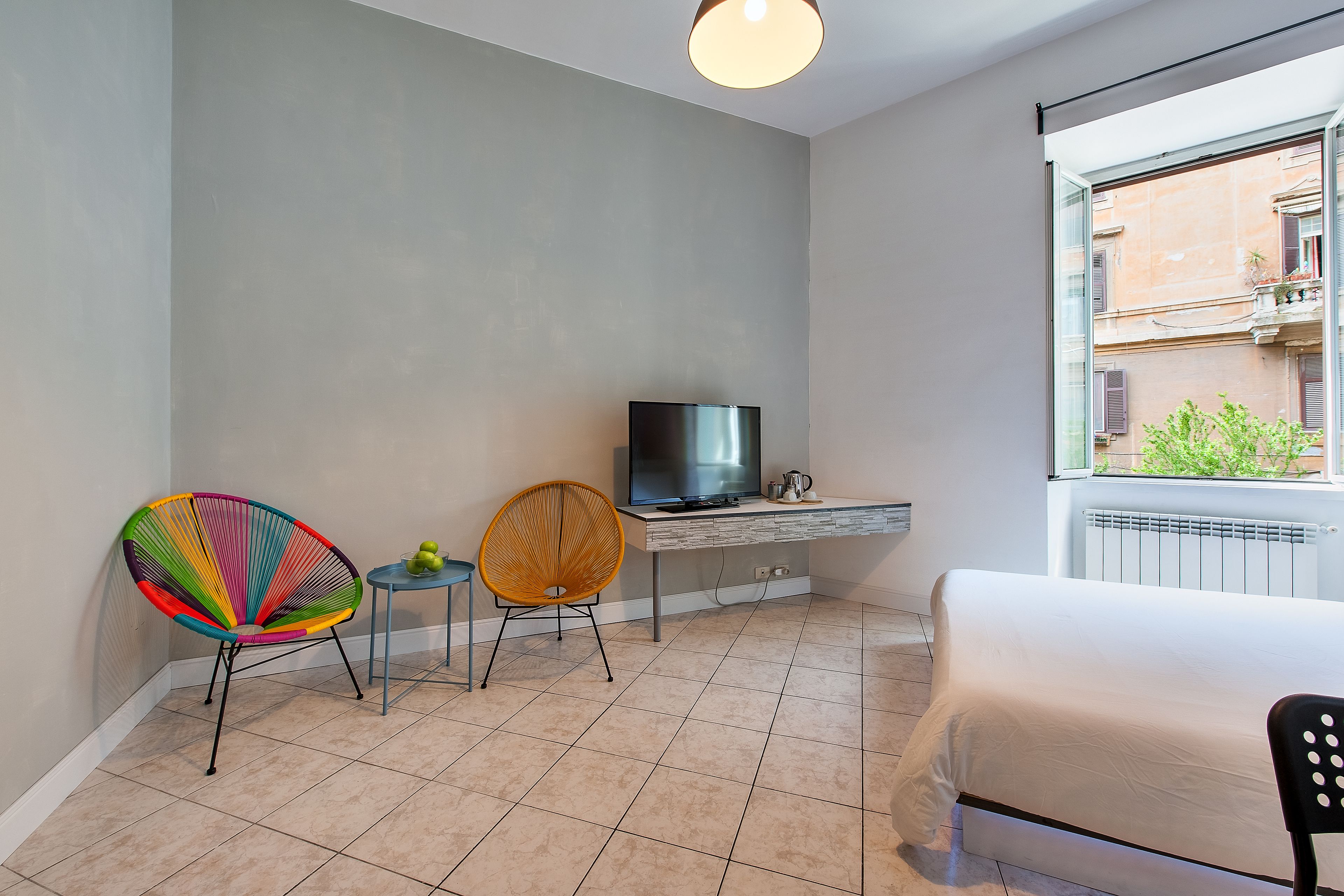 A modern hotel room with a bed, a TV, a desk, and two chairs.