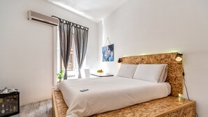 Un dormitorio con cama, aire acondicionado, mesita de noche, lámpara y ventana con cortinas.