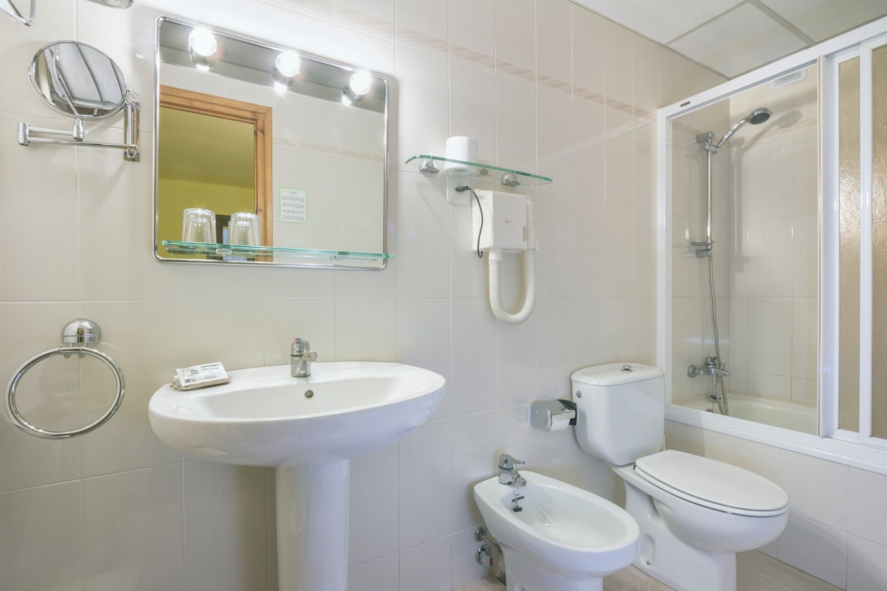 A bathroom with a sink, mirror, bidet, toilet, and shower.