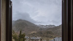Vista desde una ventana a un paisaje rural con casas, un sendero y montañas al fondo.