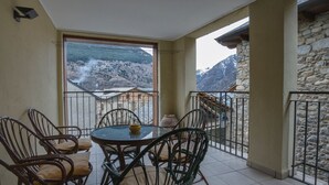 Un balcón con sillas de mimbre y una mesa, con vistas a un paisaje montañoso.