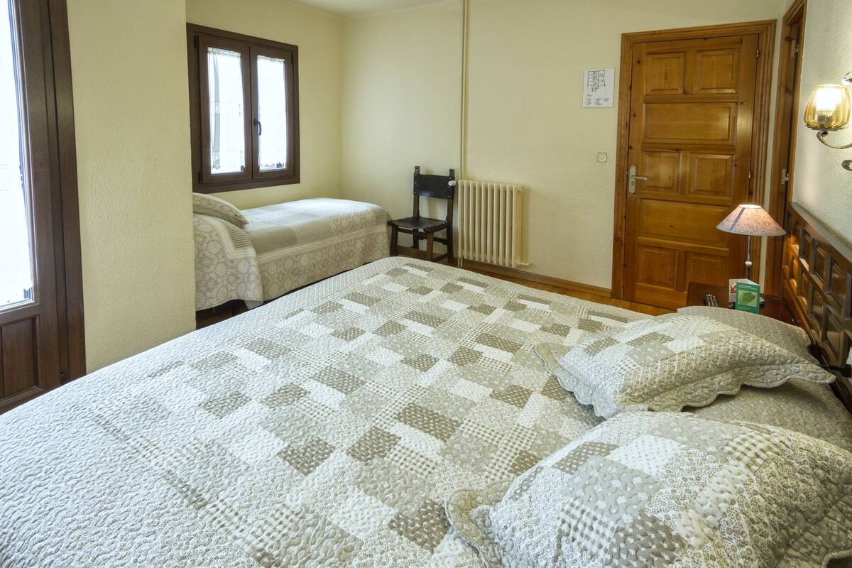Un dormitorio con dos camas individuales, una puerta de madera, un radiador y una ventana con cortinas.