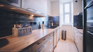 A modern kitchen with a wooden countertop, stainless steel appliances, and a black tiled backsplash. - Suite Apartments Aberdeen (Aberdeen)