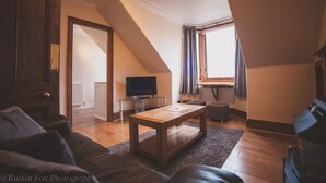 A cozy living room with a wooden coffee table, leather sofa, and a television on a glass cabinet. - Suite Apartments Aberdeen (Aberdeen)