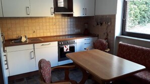 A compact kitchen with white cabinets, a wooden countertop, a stove, and a dining table with two chairs. - Ferienwohnung Auszeit (Wiehl)