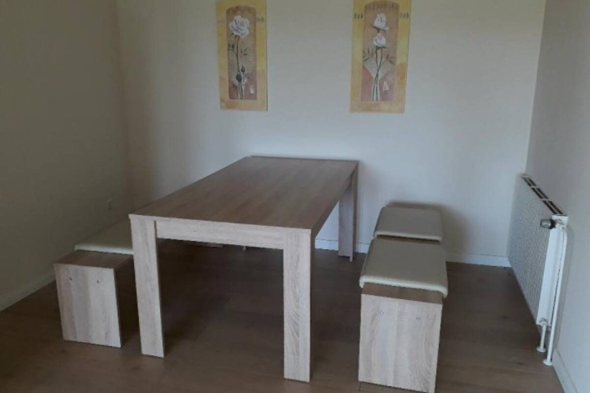 A room with a wooden table and benches, a radiator, and two wall-mounted artworks.