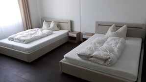 A hotel room with two single beds, each with a wooden headboard and white bedding. There are bedside tables with drawers and a small nightstand between the beds. - Ferienwohnung Auszeit (Wiehl)