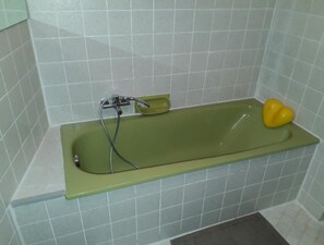 Ein Badezimmer mit einer grünen Badewanne, einem gelben, herzförmigen Gegenstand am Rand und einem Wasserhahn mit einem Schlauch.