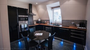 Une cuisine moderne avec un coin repas, comprenant un four encastré, un four à micro-ondes et une cuisinière, une grande fenêtre et un plan de travail de couleur sombre.