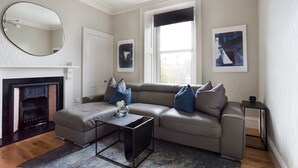 Un salon moderne avec un canapé d’angle, une cheminée, un miroir rond et des œuvres d’art accrochées aux murs.