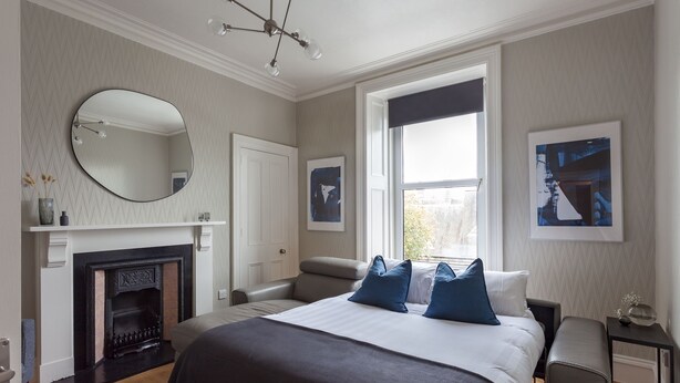 Une chambre à coucher avec un grand lit, une cheminée, une fenêtre donnant sur un beau paysage et un lustre.