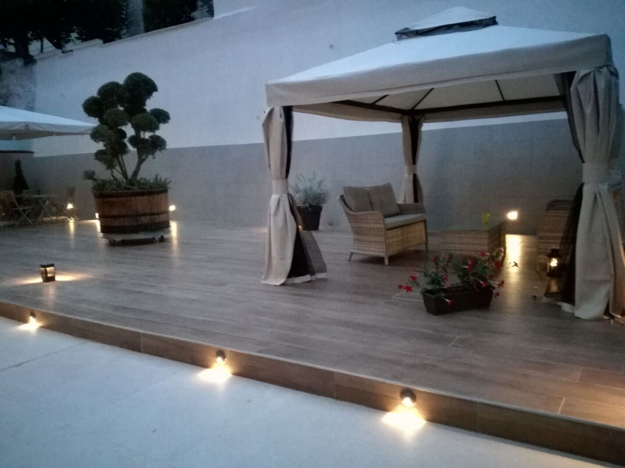 Un patio al aire libre con una zona de estar cubierta, plantas en macetas e iluminación ambiental.