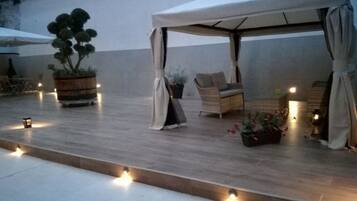 Un patio al aire libre con una zona de estar cubierta, plantas en macetas e iluminación ambiental.