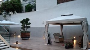 An outdoor patio area with a wooden deck, a covered seating area with a table and chairs, and a potted plant. - Buono BB (Naples)