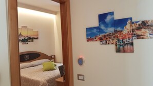 A bedroom with a bed, a nightstand, a wall-mounted light, and a thermostat. - Buono BB (Naples)