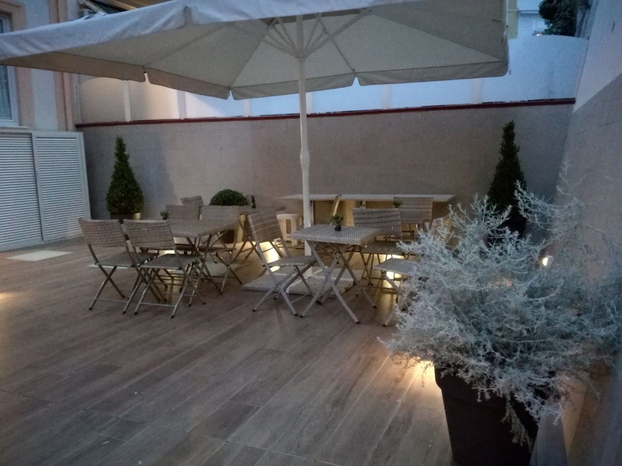 Zona patio all'aperto con sedie e tavoli pieghevoli, un ombrellone grande e piante ornamentali.